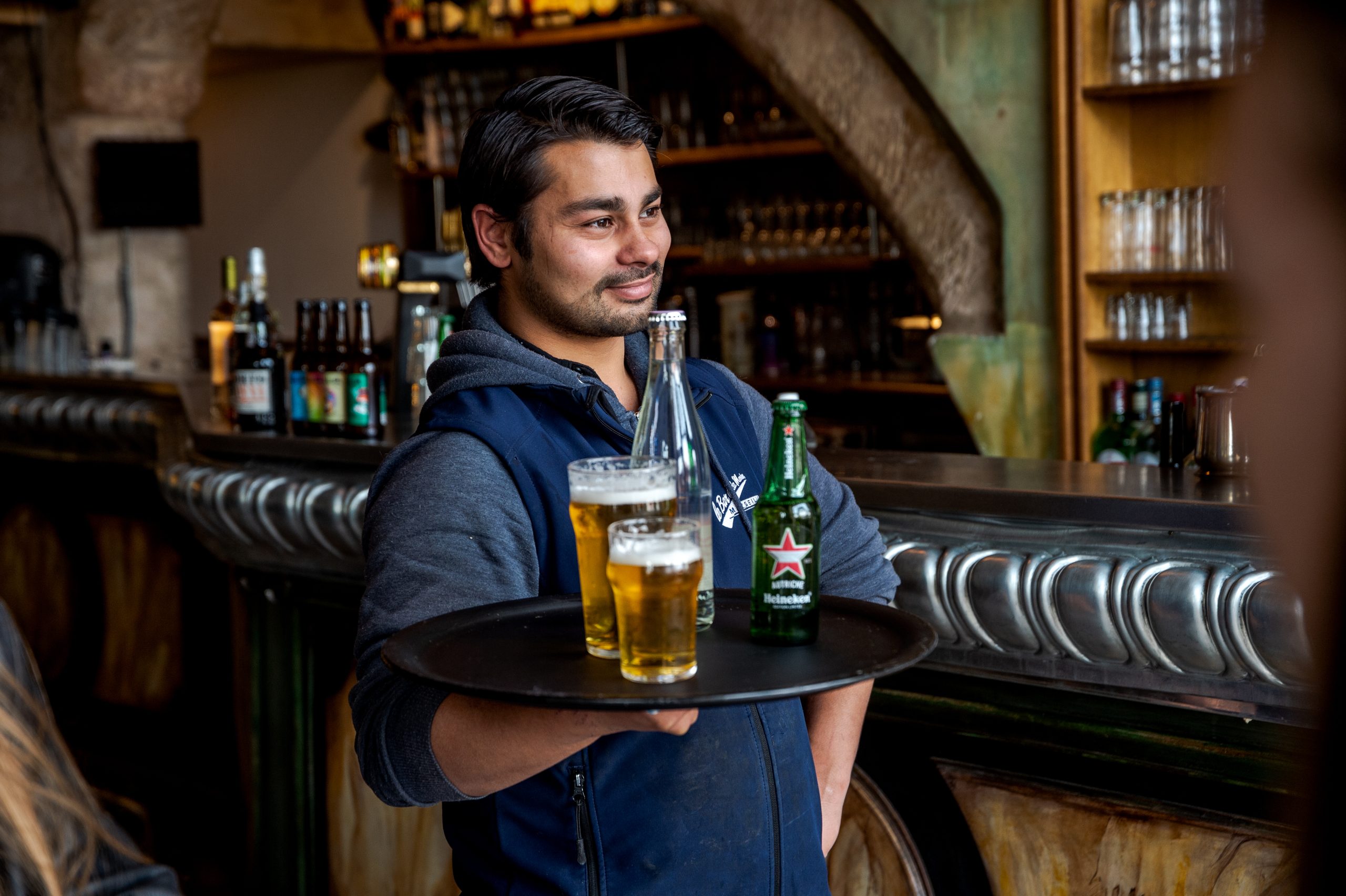 Une serveuse souriante sert une bière à un consommateur en terrasse